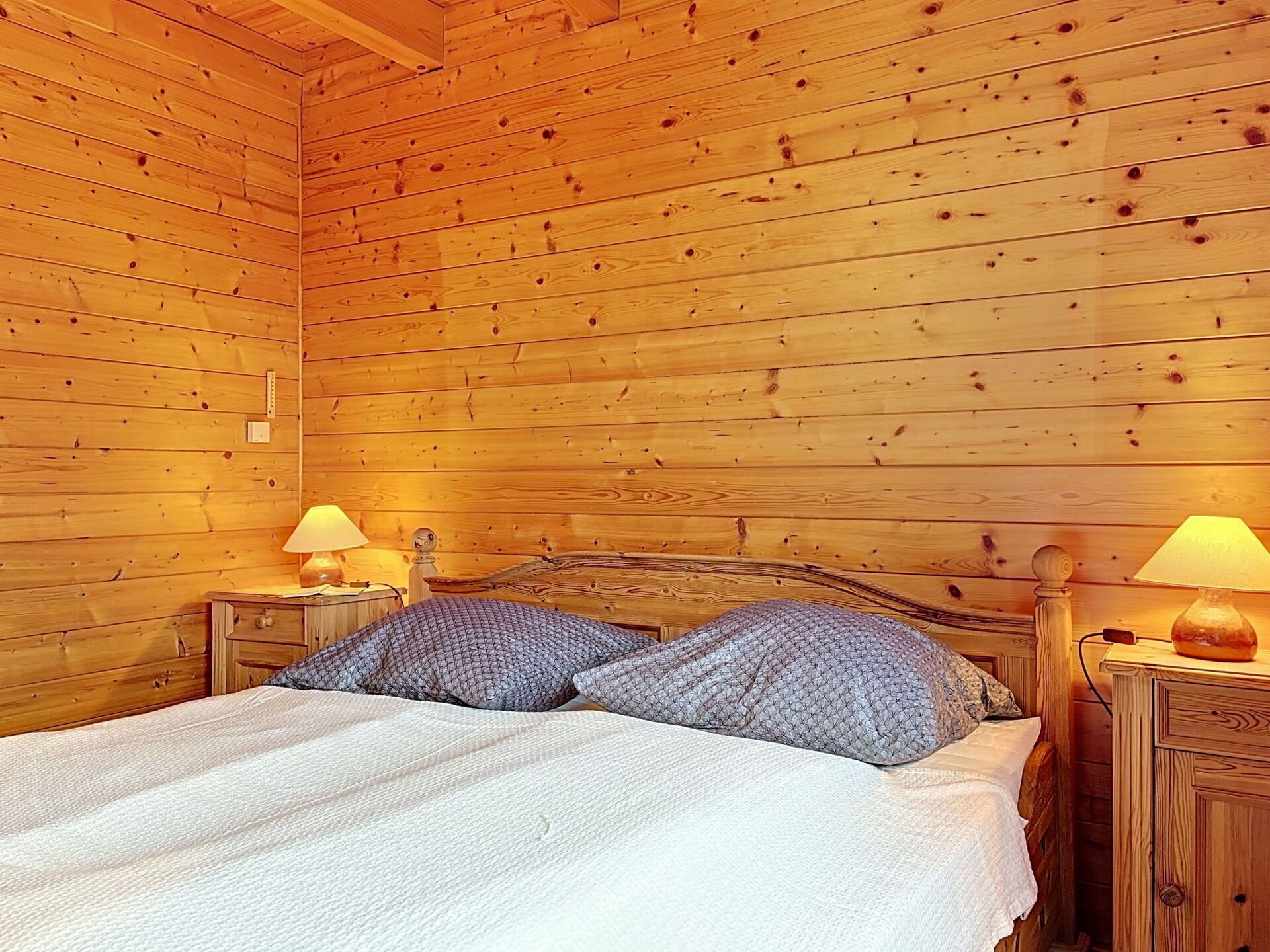 Une chambre de style cabane en bois, avec un lit, deux tables de chevet et deux lampes.