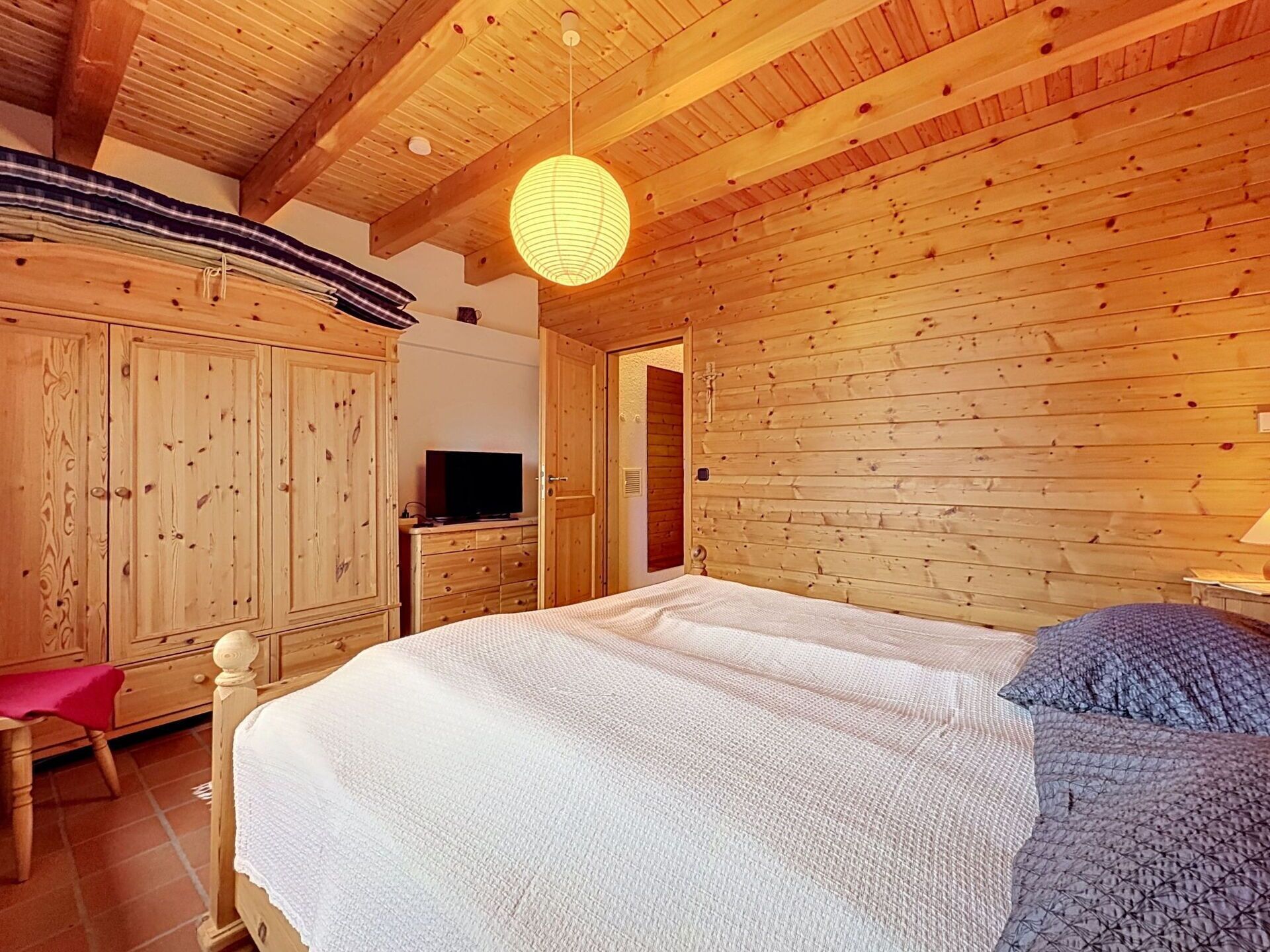 Ein Zimmer mit Holzboden, einem Bett, einem Fernseher auf einer Kommode und einer Pendelleuchte.