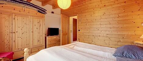 Ein Zimmer mit Holzboden, einem Bett, einem Fernseher auf einer Kommode und einer Pendelleuchte.