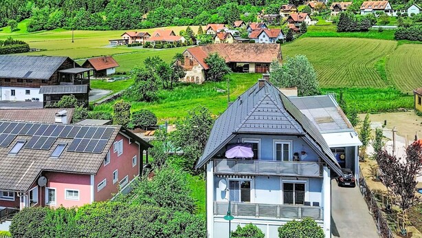 Ett bostadsområde med hus, en framträdande byggnad med ett sluttande tak och ett grönskande landskap.