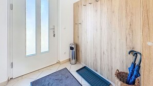 Ett rum med en dörr, en papperskorg, en matta och en korg av rotting med ett paraply i.