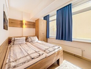 Ein Schlafzimmer mit einem hölzernen Bett, einem Nachttisch, einem Kleiderschrank, einem Fenster mit Vorhängen und einer Wandlampe.