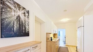 En smal hall med ett köksutrymme som har en träbänkskiva, skåp och ett kylskåp.