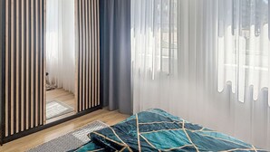 A bedroom with a bed, a sliding door, a window with curtains, and a view of the outside.