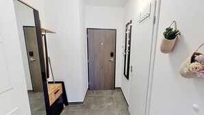A hallway with a wooden door, a mirror, a wall-mounted plant, and a small basket with flowers.