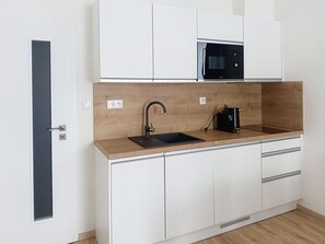 A modern kitchen with white cabinets, a wooden countertop, a black sink, a microwave, and a coffee maker.