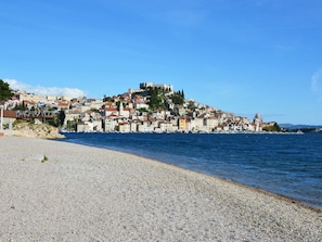 Eine Küstenstadt mit Gebäuden an einem Hügel, einem Strand im Vordergrund und einem klaren, blauen Himmel.