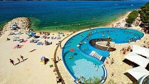 Una platja amb una gran piscina, gandules i ombrelles.