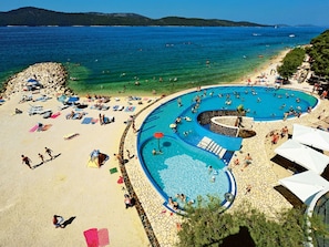 Ein Strand mit großem Pool, Liegestühlen und Sonnenschirmen.