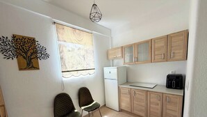A compact kitchen with two chairs, a refrigerator, wooden cabinets, and a wall-mounted light fixture. - MeThea SeaView Apartments by Greek Pride (Kassandra)