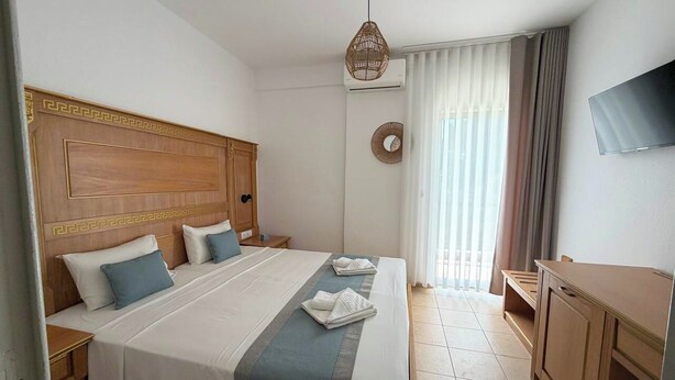 A hotel room with a large bed, a wooden headboard, a desk, a TV, and a window with curtains. - MeThea SeaView Apartments by Greek Pride (Kassandra)