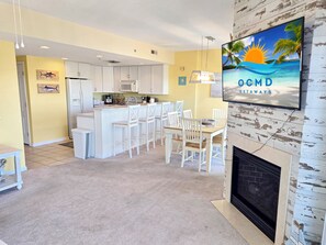 Eine moderne Küche mit weißen Schränken, einer zentralen Kochinsel und einem Essbereich mit weißen Stühlen. An der Wand befindet sich ein Flachbildfernseher, der 'OCMD GETAWAYS' anzeigt.