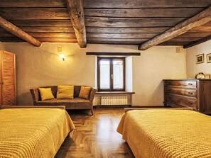 Ein Zimmer mit Holzbalken, einem Korbssessel, zwei Betten mit gelber Bettwäsche, einem Schminktisch und einem Fenster mit Blick.
