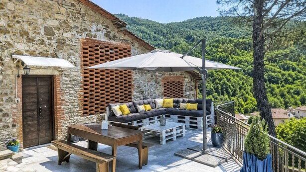 Ein Steinhaus mit Ziegelwand, einer Holzbank, einem Tisch und einer Couch mit Kissen.
