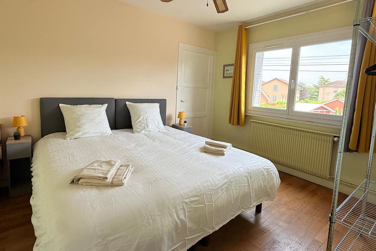 Ein Schlafzimmer mit einem Bett, zwei Nachttischlampen, einem Deckenventilator, einem Fenster mit Vorhängen und einer Heizung.