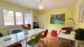 A dining area with a white table, red chairs, a laptop, and a painting on the wall. - Les appartements de katia  (Charnay-lès-Mâcon)