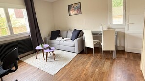 A modern living room with a grey sofa, a small round table, a white chair, and a radiator. - Les appartements de katia  (Charnay-lès-Mâcon)