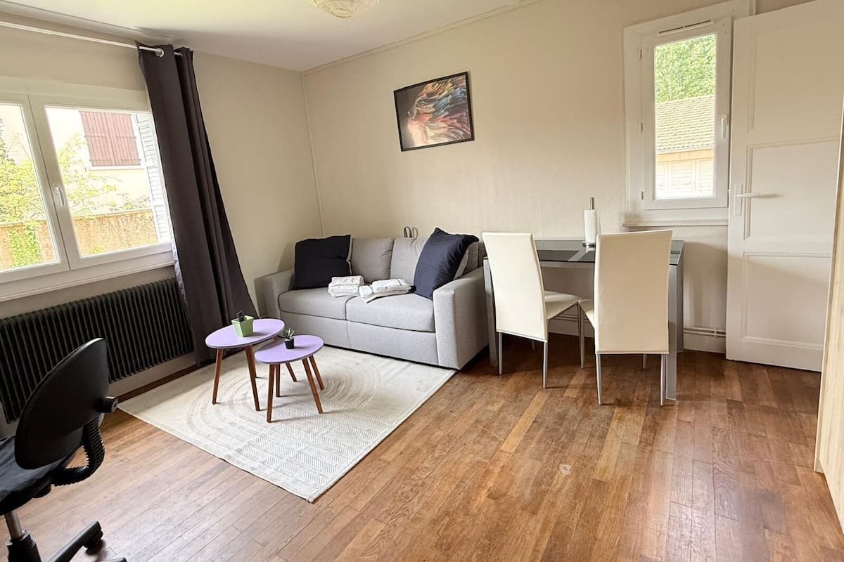 Ein modernes Wohnzimmer mit einem grauen Sofa, einem kleinen runden Tisch, einem weißen Sessel und einer Heizung.