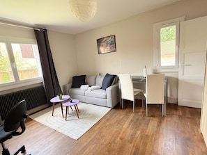 A modern living room with a grey sofa, a small round table, a white chair, and a radiator. - Les appartements de katia (Charnay-lès-Mâcon)