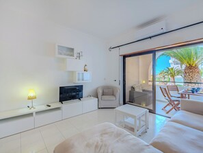 A modern living room with a flat-screen TV, a sofa, a chair, a small table, and a balcony with outdoor furniture. - Be My Guest by Interhome (Porches)