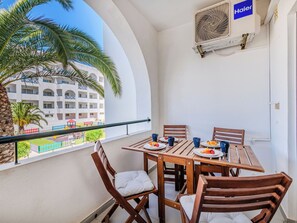 Ein Balkon mit einem Holztisch, Stühlen und Blick auf ein Gebäude mit Balkonen.