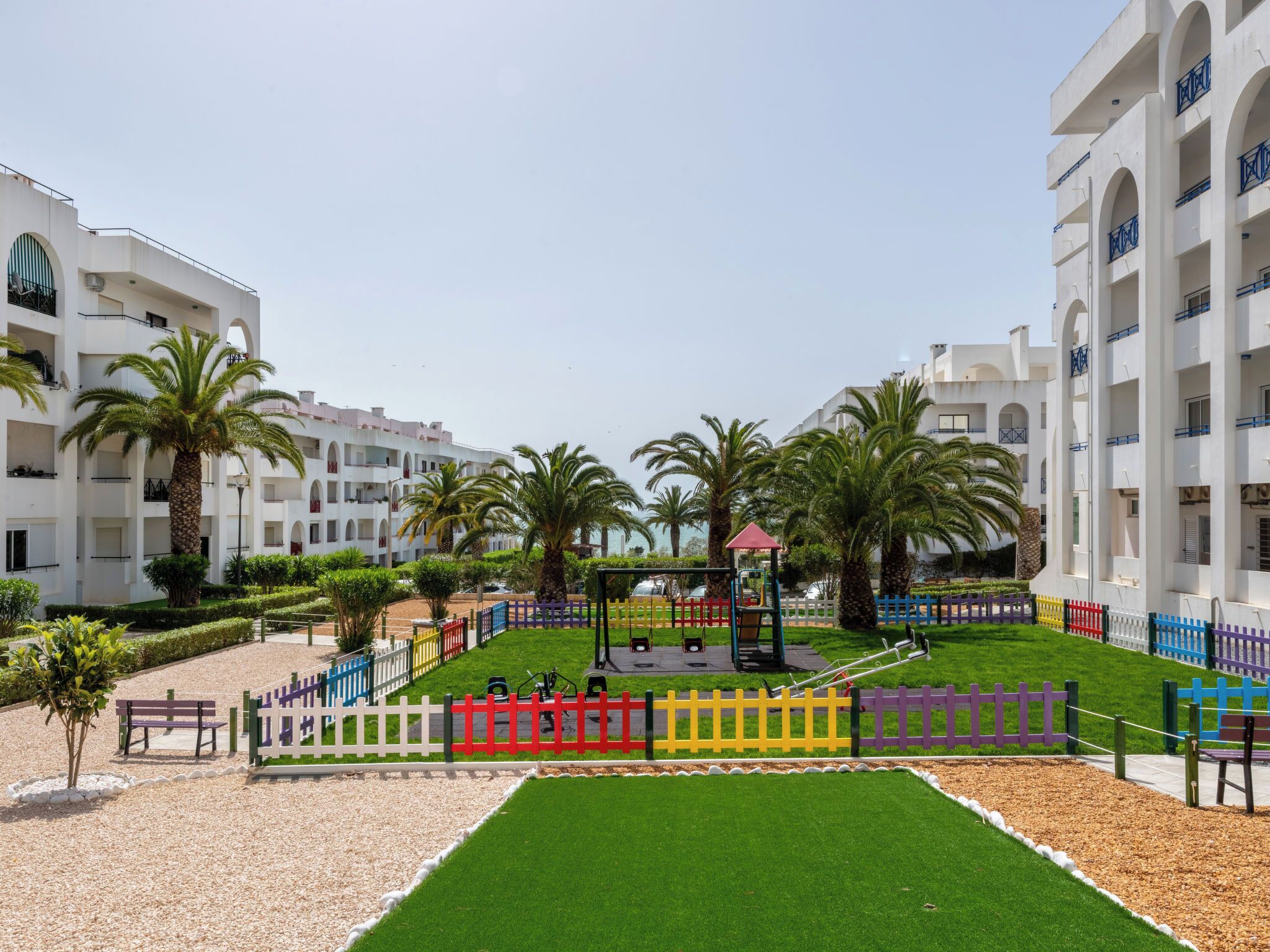 A courtyard with palm trees, a playground, and a white building with balconies.