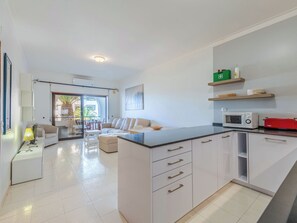 A modern kitchen with white cabinets, a central island, and a dining area with a sofa and table. - Be My Guest by Interhome (Porches)