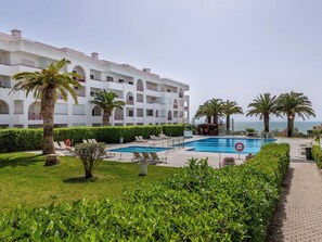 Ett hotell med en swimmingpool, palmer och utsikt över havet.