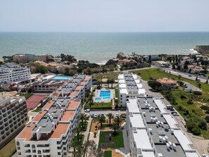 Ett bostadsområde vid kusten med hyreshus, en swimmingpool och utsikt över havet.