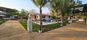A small house with a pool, surrounded by palm trees and a paved walkway.