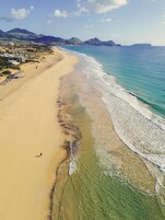 Una playa con aguas cristalinas, una orilla arenosa y montañas a lo lejos.