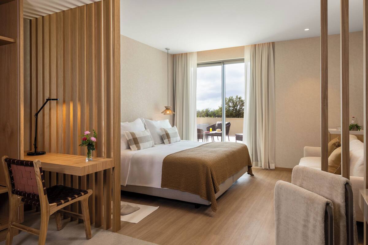 A hotel room with a bed, a desk, a chair, a table, and a view of the outdoors.