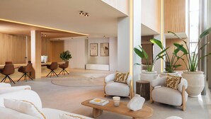 A spacious lobby with a modern design, featuring a seating area with sofas and chairs, a coffee table, and large potted plants. - Legacy Ithos Boutique Hotel (Porto Santo)
