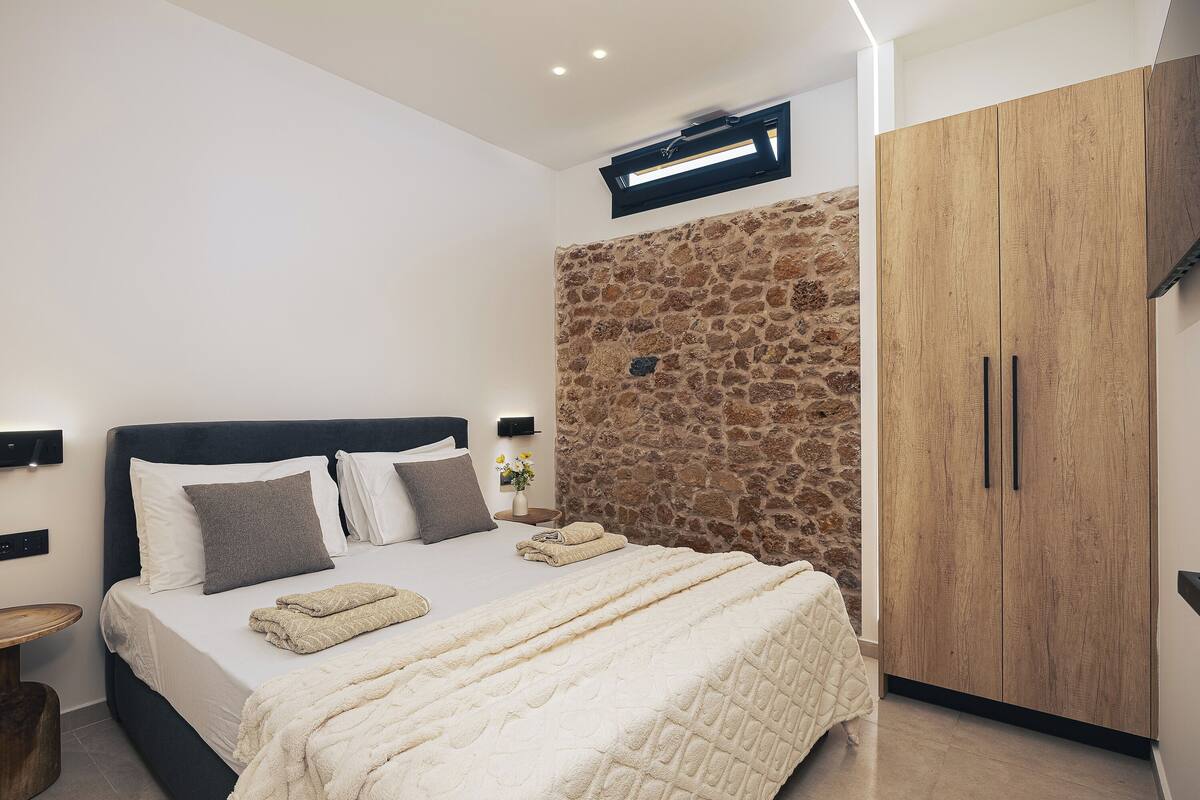 A bedroom with a bed, a stone wall, a wardrobe, and a nightstand.