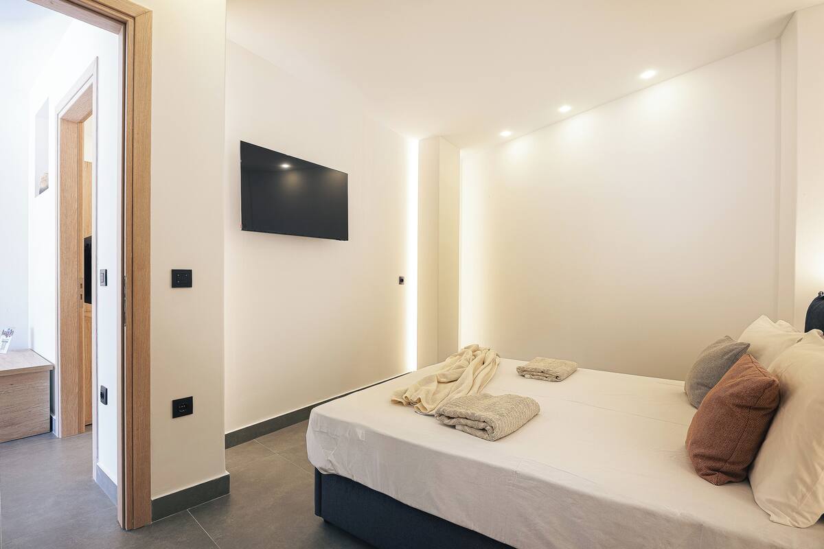 A modern bedroom with a bed, pillows, and a flat-screen TV on the wall.