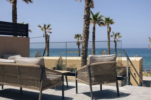 Un balcón con mobiliario de mimbre, vista al mar y palmeras.