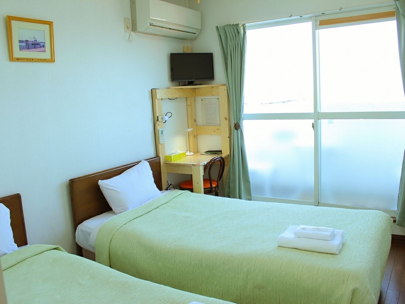 A hotel room with two beds, a desk with a chair, a television, and a window with curtains.