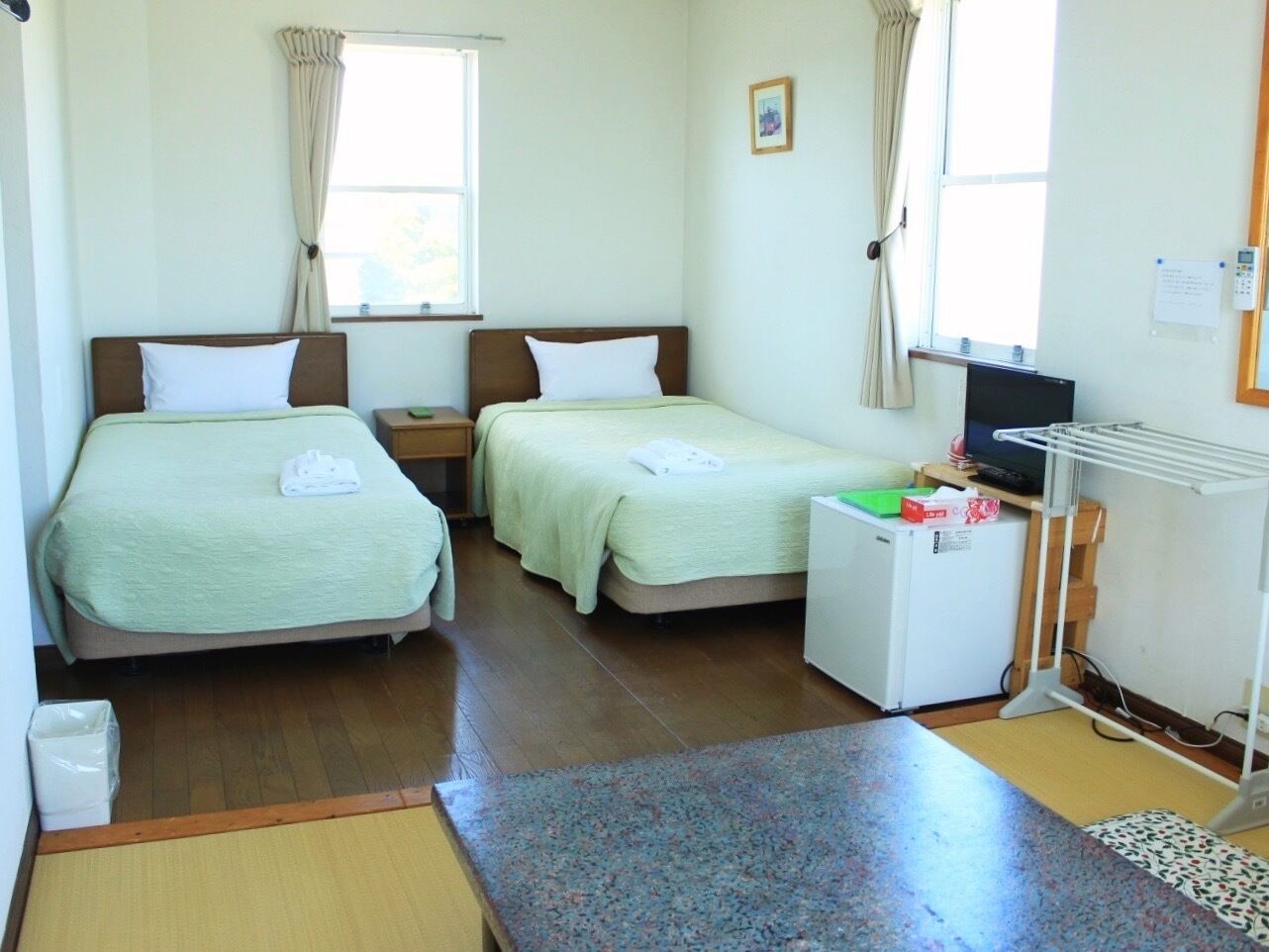 A hotel room with two beds, a small refrigerator, a desk with a computer, and a window with curtains.
