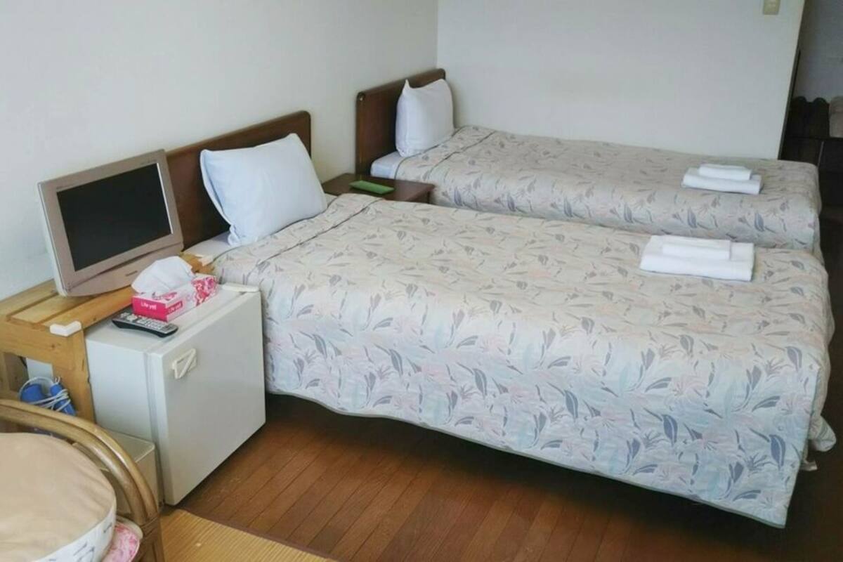 A hotel room with two beds, a small desk with a television, and a chair.