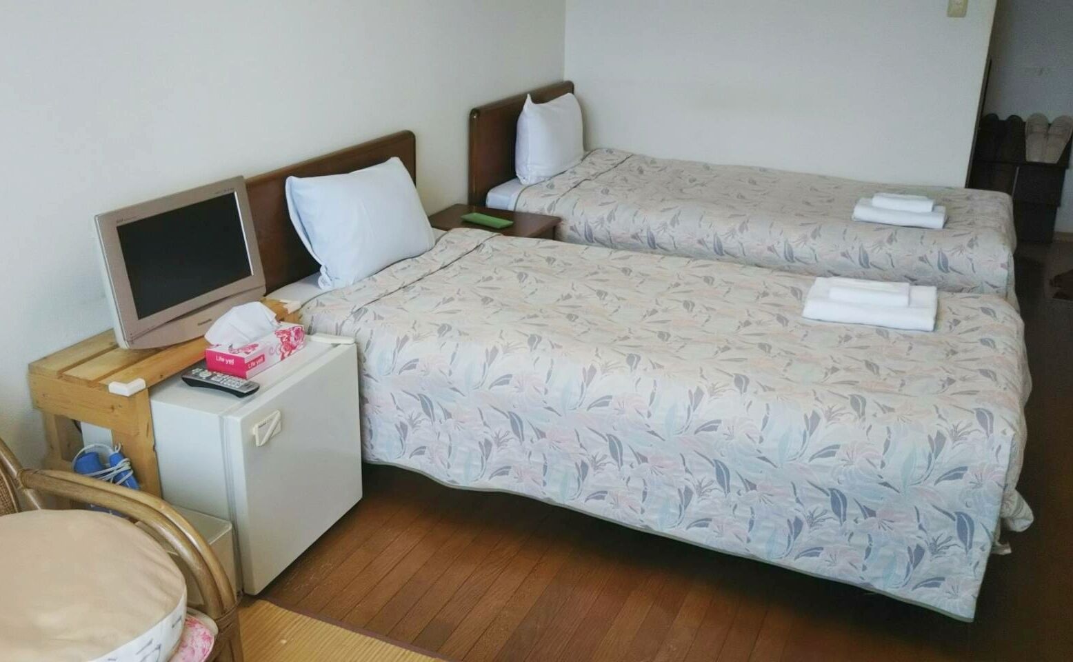 A hotel room with two beds, a small desk with a TV, a mini fridge, and a chair.