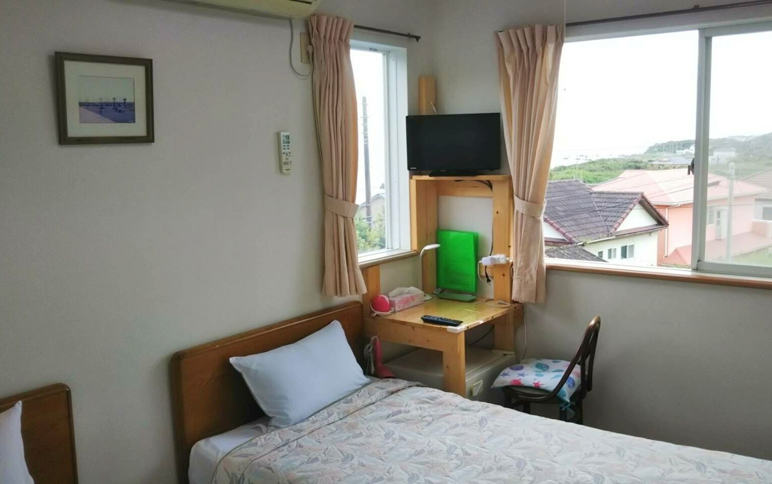 A hotel room with a bed, a desk with a computer and a TV, a chair, and a window with a view of buildings.