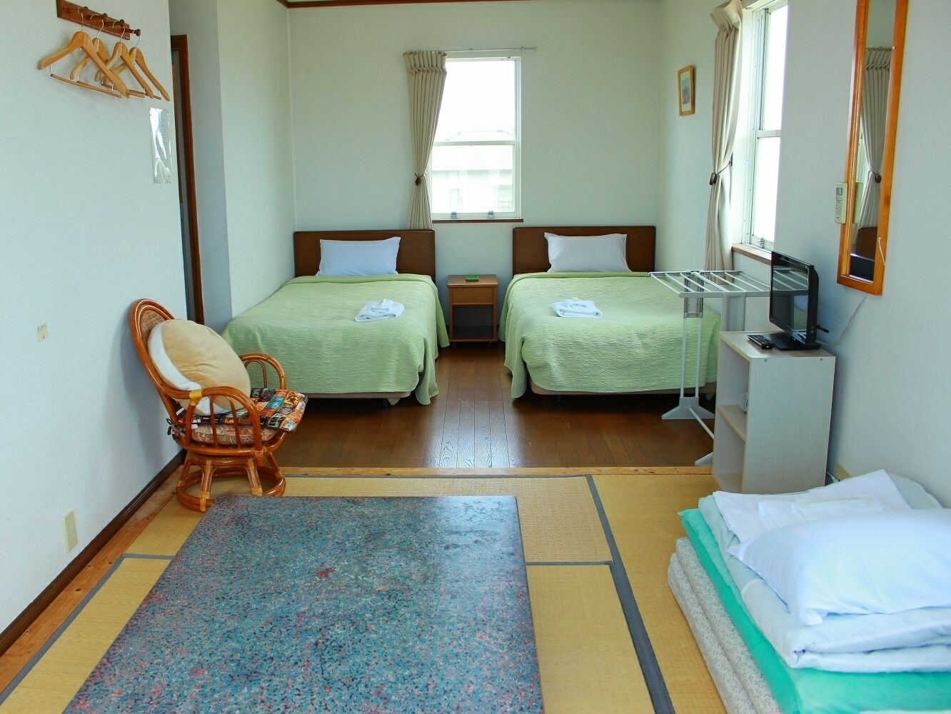 A room with two beds, a chair, a small table, and a TV.