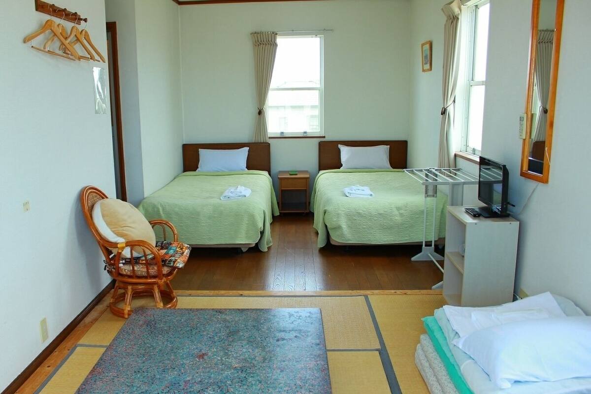 A room with two beds, a chair, a small table, and a TV.