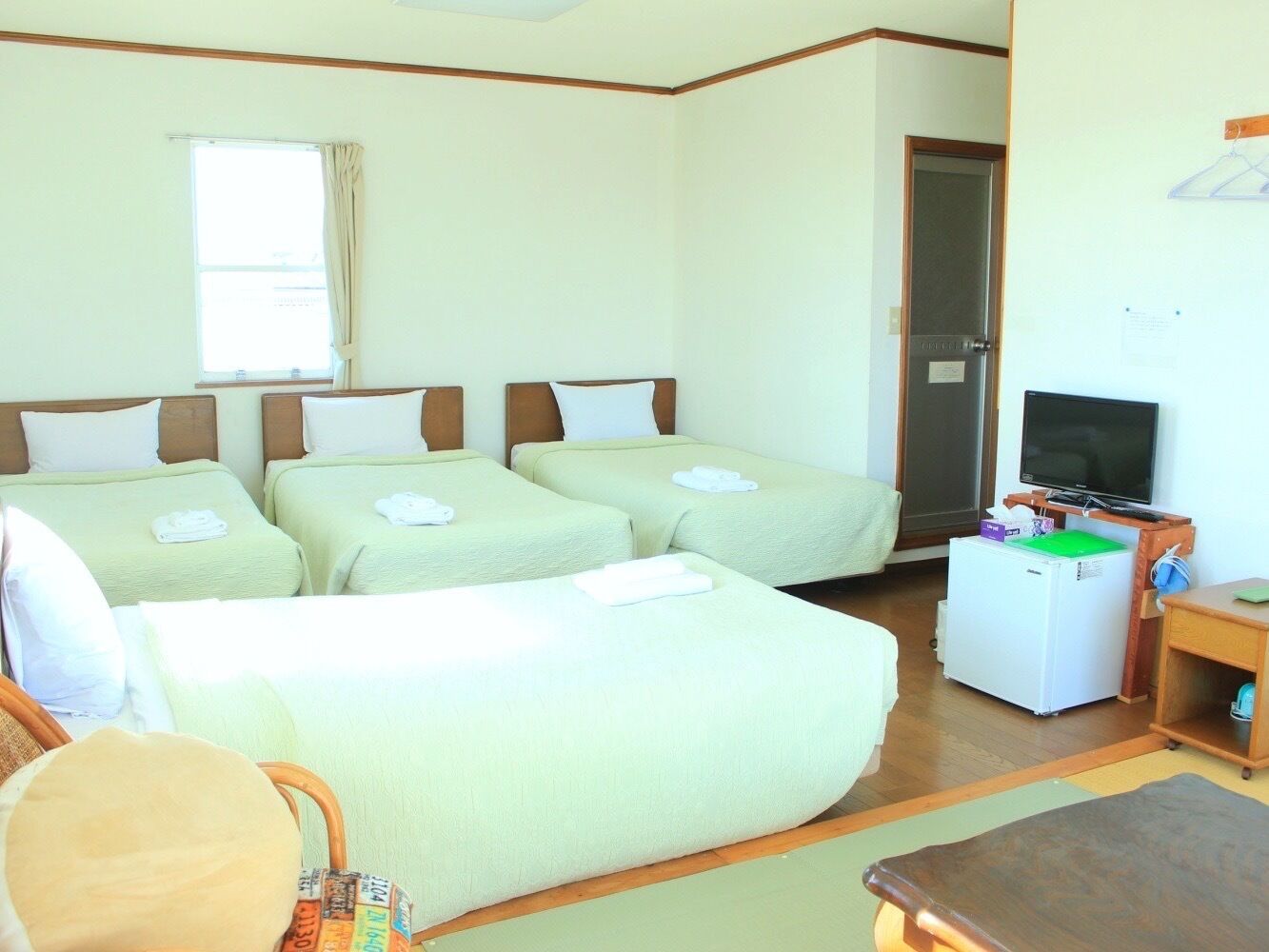 A hotel room with four beds, a television, a refrigerator, and a desk.