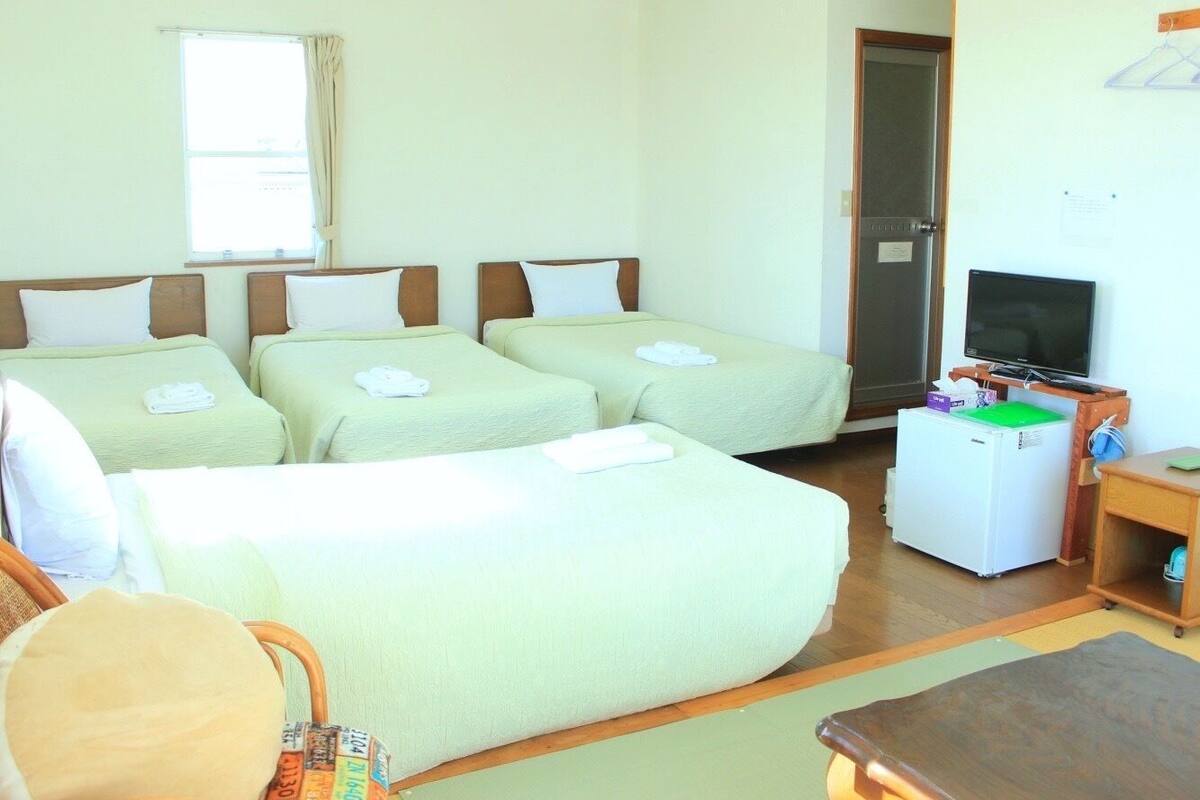 A hotel room with four beds, a television, a refrigerator, and a desk.