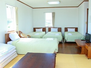 Una habitació d'hotel amb quatre llits individuals, un escriptori de fusta, televisió i una finestra amb cortines.
