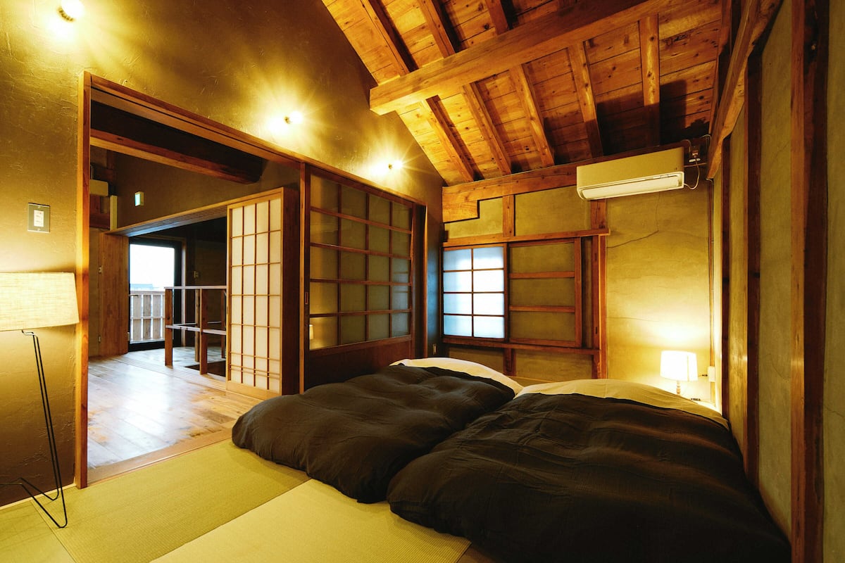 A traditional Japanese room with tatami flooring, a low bed, sliding doors, and a ceiling fan.