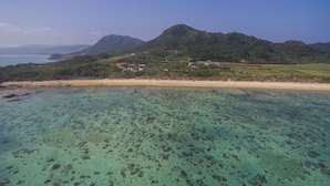 A coastal landscape with clear waters, a sandy beach, and a hill with buildings. - The Seven Stars Resort (Ishigaki)