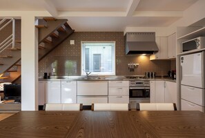 A modern kitchen with a dining area, built-in appliances, and a staircase. - Fo Sho Sanso (Kutchan)