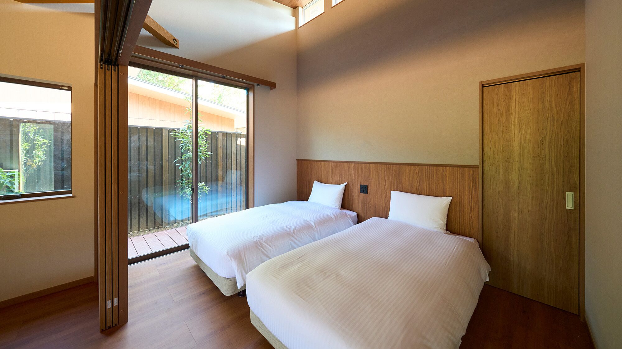 A hotel room with two beds, a wooden headboard, a sliding glass door to a balcony, and a wooden floor.